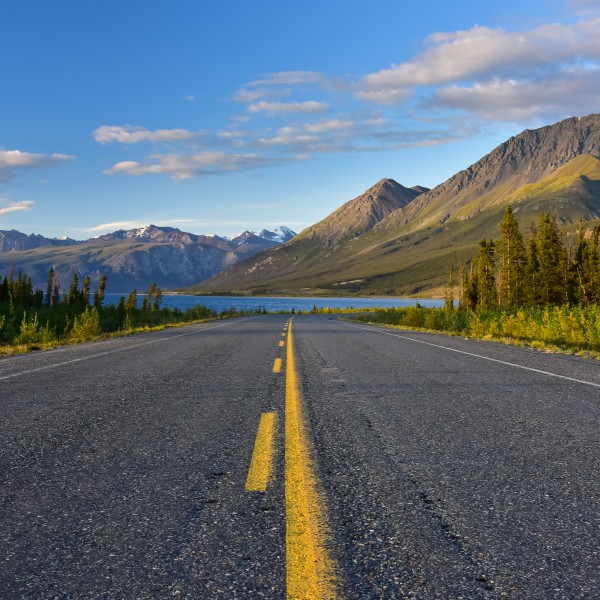 View on the road with rolling greenery and mountains against a blue sky