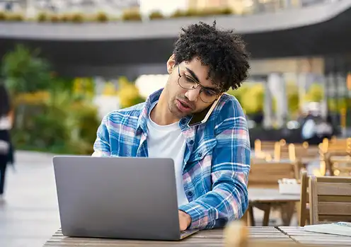 Student typing on laptop while talking on phone