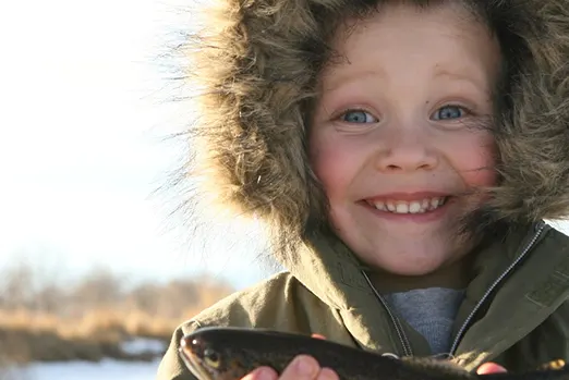 Child in a coat holding a fish.